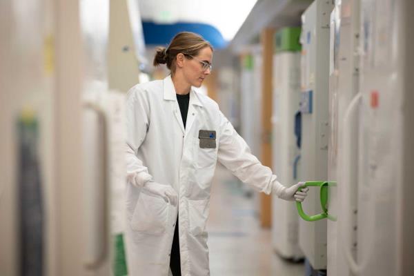 Margot Bacino wears latex gloves and white lab coat as he handles samples in Sue Lynch's lab.