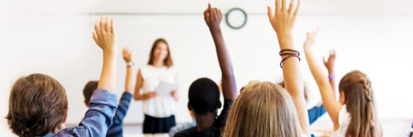 A group of school pupils with their hands up in a classroom with a teacher.