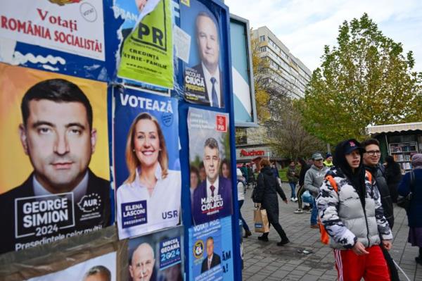 People pass by electoral posters with candidates for the presidential and parliamentary elections in Bucharest on November 22, 2024. 