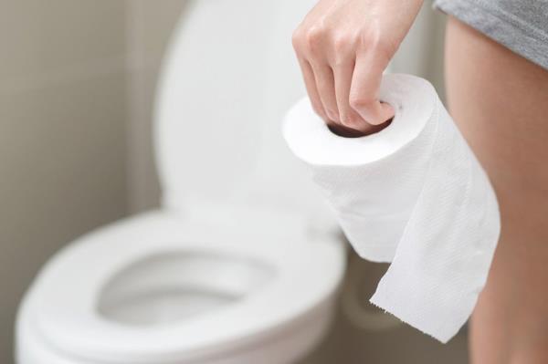 Close up of a woman walking towards the toilet holding toilet paper